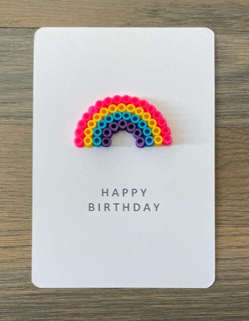 Picture of a Happy Birthday card with a small rainbow on it.  Rainbow is pink, yellow, blue, purple